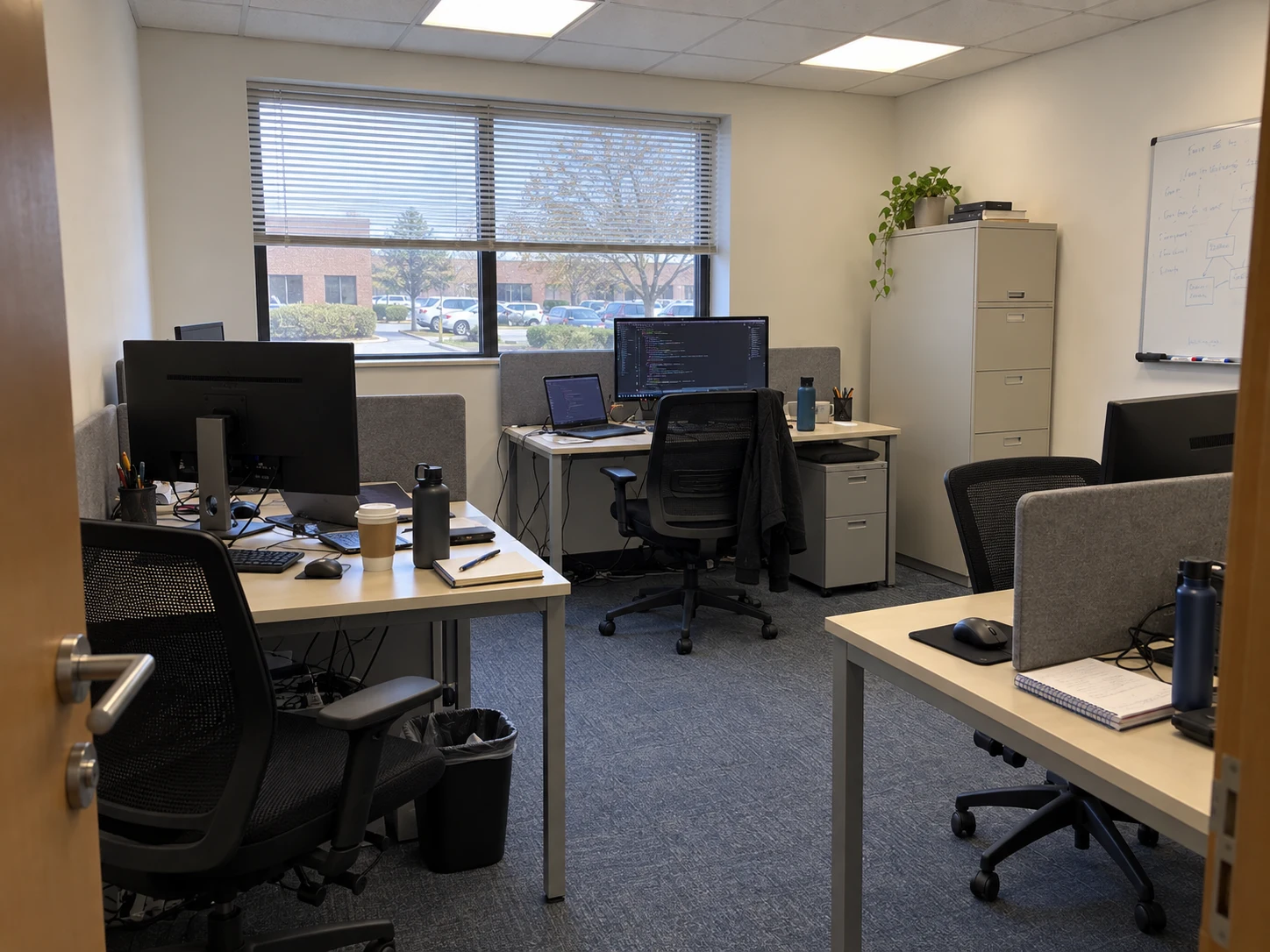 Illustrative view of a simple app development workspace, with desks, monitors and natural daylight.